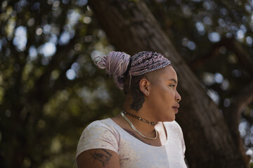 A nonbinary, Afro-Latinx model looks off to the side. Their nonbinary gender identity is alluded to by their eye-catching, bright hair and aesthetic. In the background, a forest scene is visible.