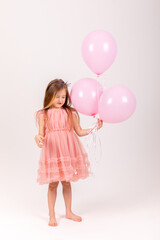 Obraz na płótnie Canvas Cute smiling little girl in a pink princess dress posing with air balloons isolated on white background. Kids Birthday party celebration concept. Happy Birthday banner with copy space. Studio shot.