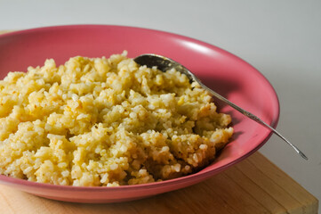 Fried rice, a typical Indonesian dish, is served on a red plastic plate and a spoon on a wooden board isolated on a white background