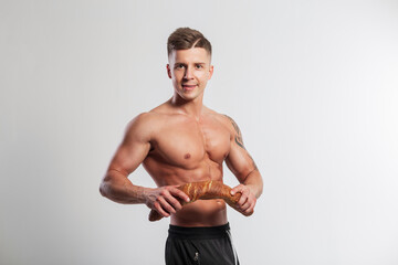 Happy handsome strong athlete fit guy with a hairstyle with a muscular body breaks a baguette bread on a white background. Healthy food and baking, concept