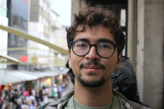 closeup portrait of young man with beard and glasses smiling with crowded city street view