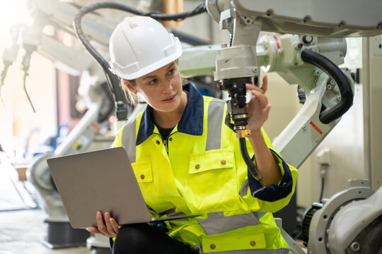 Engineer in modern industrial factory using laptop setting and inspect . robot arm controller in production plant factory.