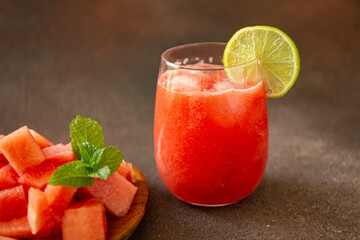 Pieces of watermelon on wood board and watermelon juice on dark brown background 