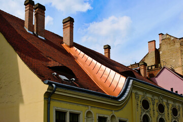 Copper flashing detail on sloped brown clay tile roof and dormer. oval rococo style window....