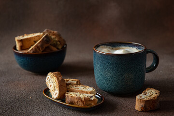 Italian biscotti with hazelnuts with a blue cup of cappuccino on a dark brown background 
