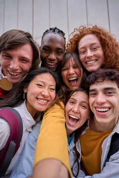 Vertical cell phone selfie of excited multiracial group of erasmus college students together outside. Cheerful smiling young friends pose laughing for photo. Happy people on campus.