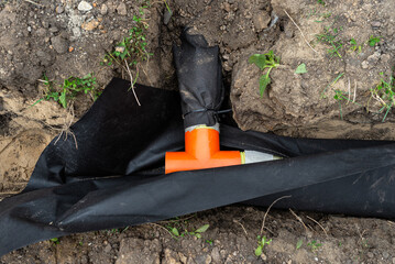 Drainage pipe wrapped in geotextile, inserted into a ditch dug around the house, visible PVC tee.