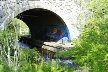 Stone arch bridge with lovely mural over the river in Brewster Gardens, a historical site and public park in Plymouth, MA.