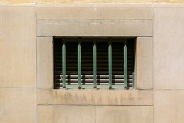 Small rectangular window on a stone wall, covered with green metal bars. From the Window of the World series.