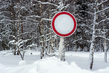 Road sign "No motor vehicles" in a large snowdrift against the backdrop of a winter forest.