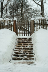 Stone steps with snowdrifts on the edges leading to a wooden gate in the fence.