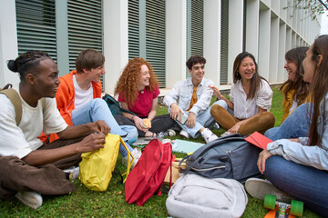 Group cheerful students gathered together outdoors. Multiracial college classmates enjoy recreation sitting on grass in campus garden. Concept of companionship and togetherness among young people.