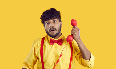 Funny man talking on retro telephone. Indian guy in yellow shirt with red bow tie holding red...