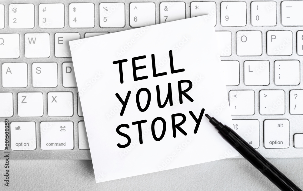 Poster white paper with text tell your story lying on the keyboard