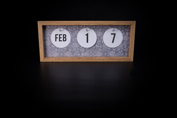 A wooden calendar block showing the date February 17th on a dark black background, save the date or date of an event concept.