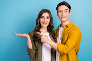 Gordijnen Portrait of two astonished people students demonstrate hold arm new proposition cheap family insurance empty space isolated on blue color background © deagreez