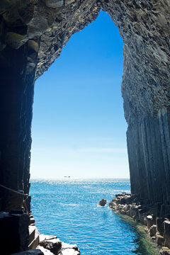 Iona island seen from the inside of the famous Fingal's Cave at Staffa island, dark basalt columns against blue summer sky, Inner Hebrides, Scotland.