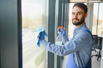 Young man cleaning window in office