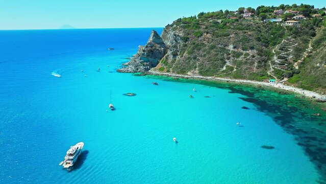View from above of crystal clear blue water on a seaside cliff in Europe in 4K. Aerial view of blue lagoon on a seashore surrounded by boots in Capo Vaticano, in Calabria, Italy.