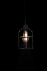 Retro lamp burning in an old iron lantern, casting rays on its walls, isolated on a black background