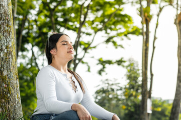 latina woman thinking and meditating in the middle of nature, raising her head to get some fresh air