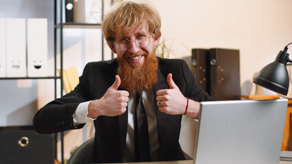 Like. Happy young bearded businessman guy working on laptop looking approvingly at camera showing thumbs up, like sign positive something good, positive feedback at office workplace. Freelancer man