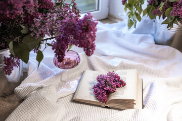 Bouquet of lilacs on the table with a cup of black tea, a croissant and an open book