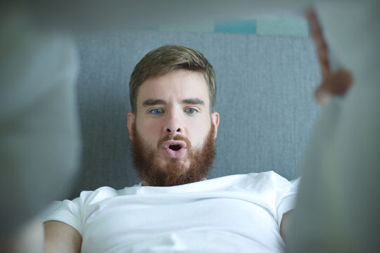 Young happy man looking at his penis under blanket, surprised guy is having good morning potency, erection in bed in bedroom 