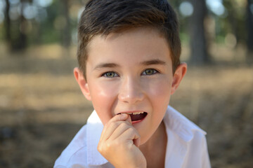 A boy-child, with his mouth open, holds on to a baby tooth, showing that he is staggering. Portrait of a brave boy 7 years old shaking baby tooth. Change of teeth in children. Self-medication at home