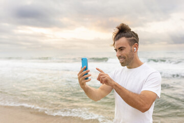 long-haired man touching mobile phone screen smiling while wearing headphones talking on phone listening to music