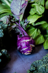 purple kohlrabi in natura with other vegetables around, on a gray surface © Luca
