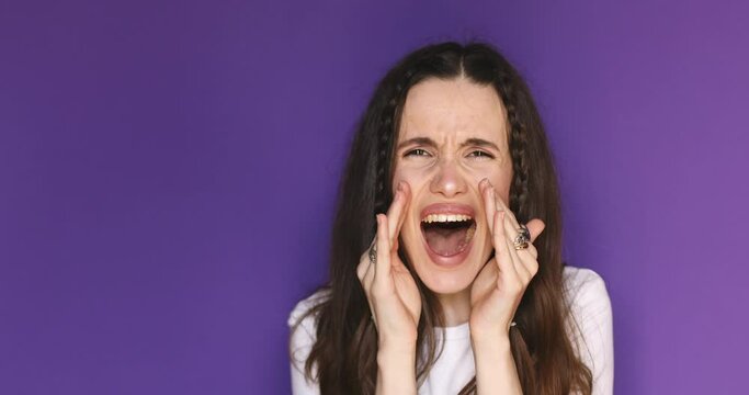 Angry sad brunette young woman with braids in white long sleeves posing isolated on purple background studio. Woman shout screaming news with hands near mouth shocked wow.