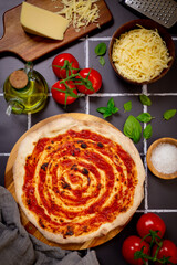 baked pizza with tomato sauce, with  tomatoes, mozzarella, olive oil, basil leaves, and salt on a dark surface