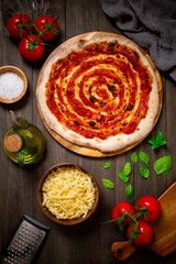 baked pizza with tomato sauce, with  tomatoes, mozzarella, olive oil, basil leaves, and salt on a dark surface