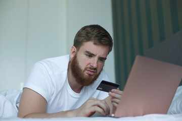 Nervous sad upset confused young man, stressed worried guy having problem with paying, buying online, payments with credit blocked bank card, looking at screen, monitor of laptop. Internet fraud