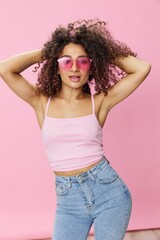 Happy woman afro curls hair dancing on pink background smile with teeth in summer pink t-shirt jeans and glasses, summer vibe, copy space