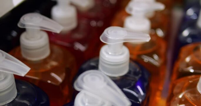 Rows unbranded transparent colorful bottles of consumer cosmetics with pumps. Unlabelled dark blue and orange shampoo or liquid soap in consumer packaging without logo.