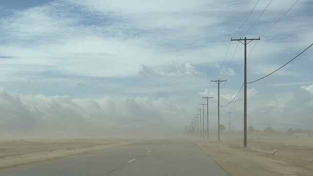 Wide view dust storm on desert highway in southern California, with telegraph poles at side of the road, fading into distance