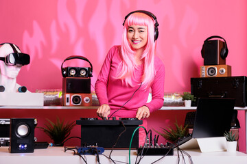 Musical performer with pink hair playing electronic song at professional turntables, enjoying performing music in club during night time. Asian musician mixing sounds in studio with isolated