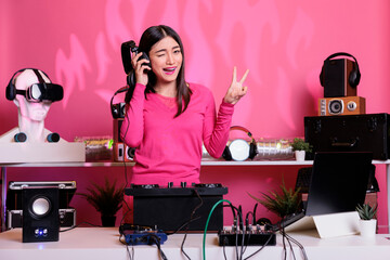Artist with pink blouse wearing headset having fun while playing techno music using mixer console,...