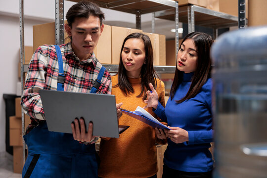 Warehouse employees managing parcel recieving and sending operation online on laptop. Storehouse managers team discussing inventory report and working together in storage room
