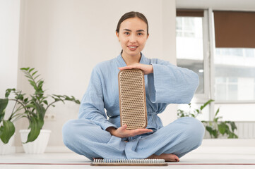 Asian woman sitting in lotus position on yoga mat and holding sadhu boards.