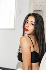 Naklejka premium medium shot of a latina teenager looking backwards sitting on the sofa of the house