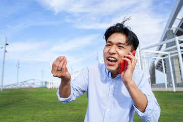 Angry young Asian man talking on cell phone. Annoyed Chinese boy argues someone on telephone. Excited male communicating. People arguing outdoors negative attitude.