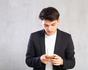 Focused young guy teenager in business clothes writes message on mobile phone