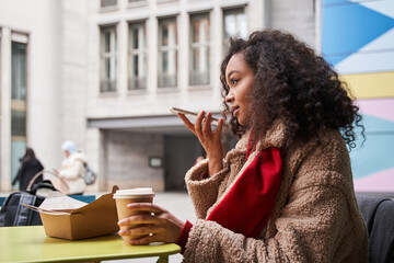 Lovely brunette woman recording voice message via mobile phone while sitting at cafe