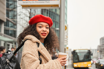 Waist up portrait of beautiful curly lady in glasses holding cup of coffee and looking camera with smile