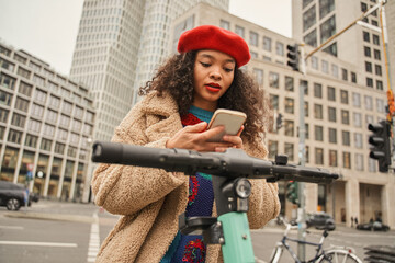 Horizontal shot of the multiracial woman using scooter sharing app at the urban street