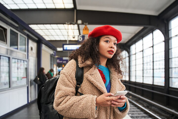 Curly brunette girl standing at the tram station and holding smartphone