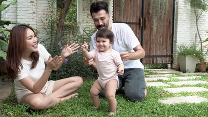 Happy asian mixed race children daughter dance on green grass with parent enjoyment laughing playful together in park. Little infant with mother father sitting dance together relax summer time garden.